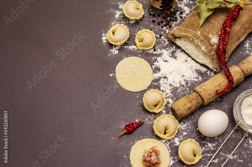 Composition with raw dumplings and ingredients on trendy black stone concrete background. Process of cooking