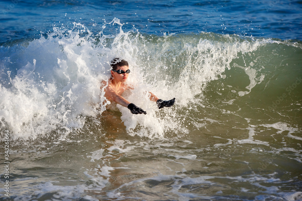 Teenager boy splashing in ocean waves. Ocean and water fun for kids.