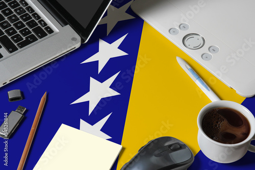 Bild auf Leinwand Bosnia Herzegovina national flag on top view work space of creative designer with laptop, computer keyboard, usb drive, graphic tablet, coffee cup, mouse on wooden table