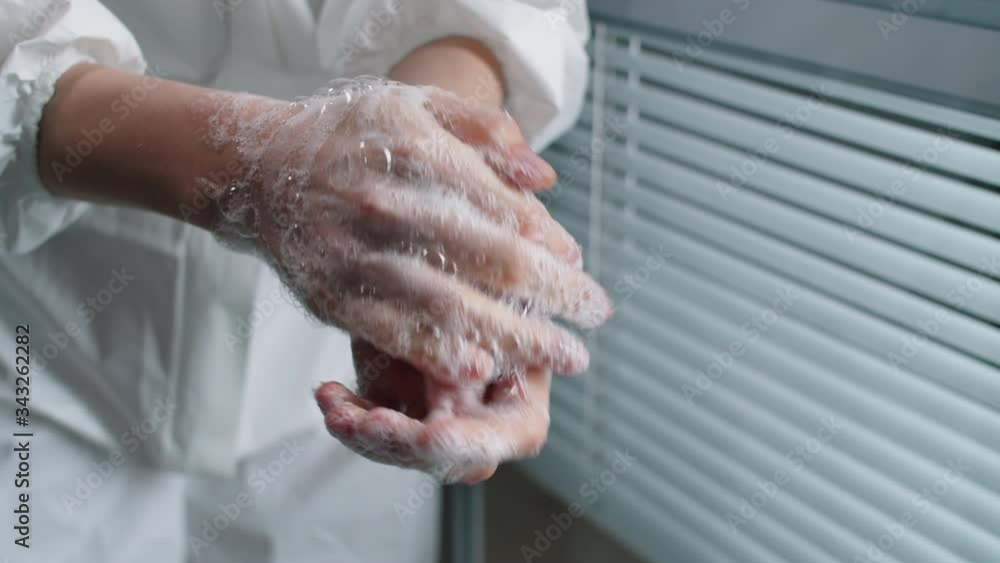Close up view of unrecognizable female doctor in lab coat lathering her hands by rubbing them together with the soap while working in hospital Close up view of unrecognizable female doctor in lab coat lathering her hands by rubbing them together with the soap while working in hospital