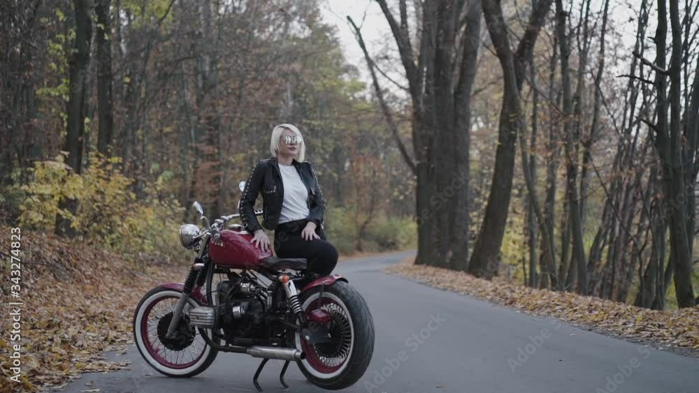 Stylish blonde leaned on retro motorbike in park, man comes to her Stylish blonde leaned on retro motorbike in park, man comes to her