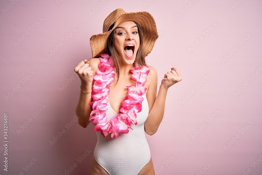 Young beautiful brunette woman on vacation wearing swimsuit and Hawaiian flowers lei celebrating surprised and amazed for success with arms raised and open eyes. Winner concept. Young beautiful brunette woman on vacation wearing swimsuit and Hawaiian flowers lei celebrating surprised and amazed for success with arms raised and open eyes. Winner concept.
