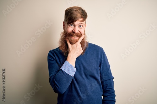 Handsome Irish redhead business man with beard standing over isolated background looking confident at the camera smiling with crossed arms and hand raised on chin. Thinking positive.
