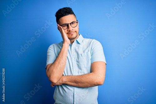 Young handsome man wearing casual summer shirt and glasses over isolated blue background thinking looking tired and bored with depression problems with crossed arms.