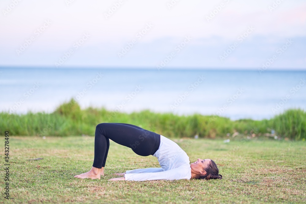 Fototapeta premium Young beautiful sportwoman practicing yoga. Coach teaching bridge pose at park