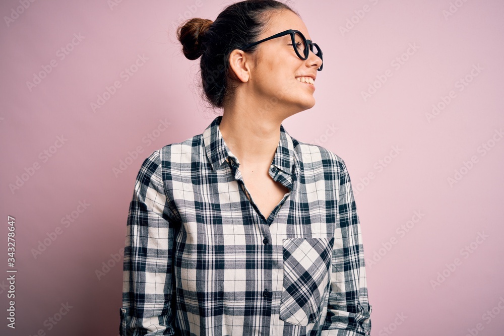 Young beautiful brunette woman wearing casual shirt and glasses over pink background looking away to side with smile on face, natural expression. Laughing confident. Young beautiful brunette woman wearing casual shirt and glasses over pink background looking away to side with smile on face, natural expression. Laughing confident.