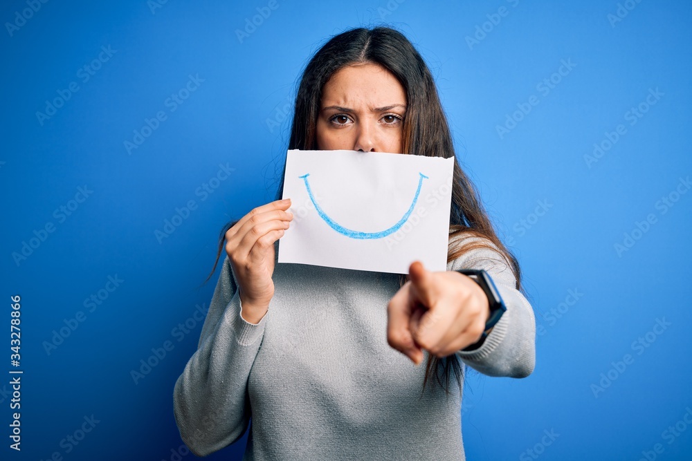 Young beautiful brunette positive woman holding card with smile emotion on mouth pointing with finger to the camera and to you, hand sign, positive and confident gesture from the front Young beautiful brunette positive woman holding card with smile emotion on mouth pointing with finger to the camera and to you, hand sign, positive and confident gesture from the front