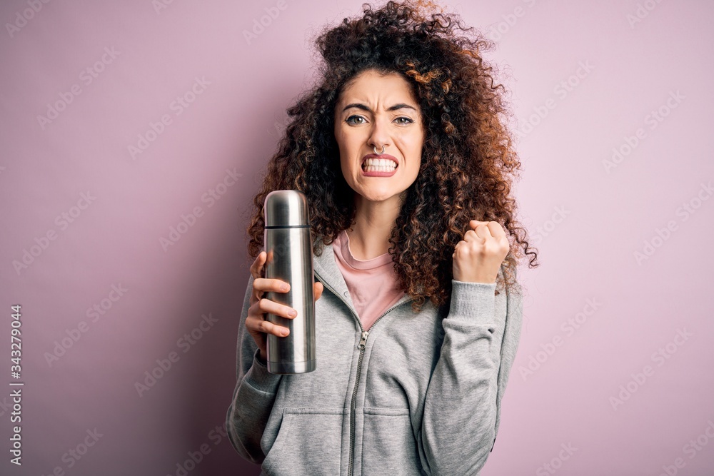 Young beautiful tourist woman with curly hair and piercing holding thermo with water annoyed and frustrated shouting with anger, crazy and yelling with raised hand, anger concept Young beautiful tourist woman with curly hair and piercing holding thermo with water annoyed and frustrated shouting with anger, crazy and yelling with raised hand, anger concept