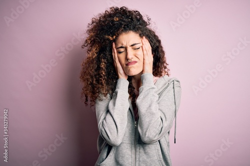 Young beautiful brunette sportswoman with curly hair and piercing wearing sportswear suffering from headache desperate and stressed because pain and migraine. Hands on head.