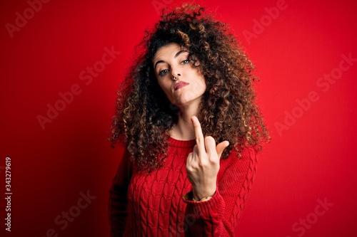 Young beautiful woman with curly hair and piercing wearing casual red sweater Showing middle finger  impolite and rude fuck off expression