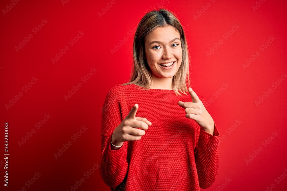 Young beautiful blonde woman wearing casual sweater over red isolated background pointing fingers to camera with happy and funny face. Good energy and vibes. Young beautiful blonde woman wearing casual sweater over red isolated background pointing fingers to camera with happy and funny face. Good energy and vibes.