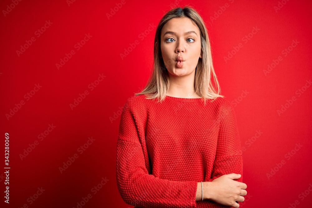 Young beautiful blonde woman wearing casual sweater over red isolated background making fish face with lips, crazy and comical gesture. Funny expression. Young beautiful blonde woman wearing casual sweater over red isolated background making fish face with lips, crazy and comical gesture. Funny expression.
