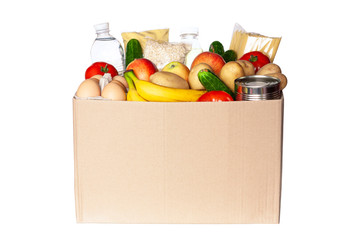 Various grocery items in cardboard box isolated on white background. Food box with fresh vegetables, fruits, cereals, pasta, milk, eggs and canned goods. Food delivery or donation concept.