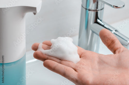 Automatic soap dispenser in the bathroom. Hand with soapy solution closeup.