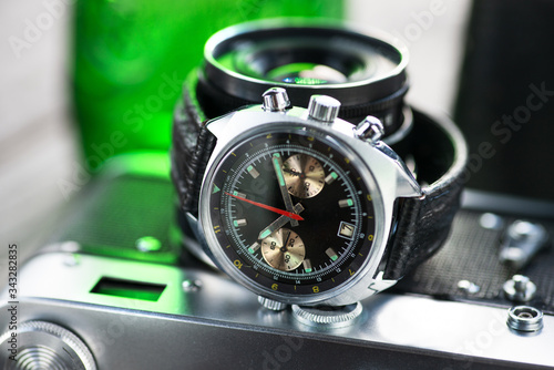 Vintage pilot chronograph watch, with black leather strap laying on film photo camera in green light. 