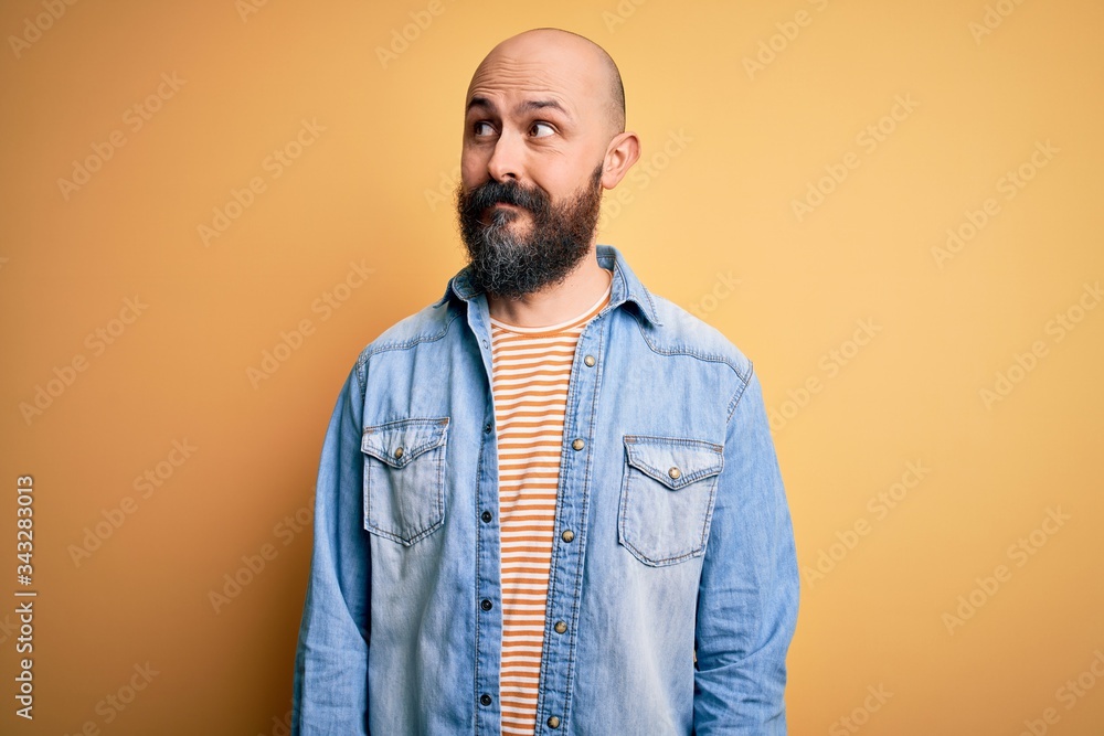Handsome bald man with beard wearing casual denim jacket and striped t-shirt smiling looking to the side and staring away thinking. Handsome bald man with beard wearing casual denim jacket and striped t-shirt smiling looking to the side and staring away thinking.