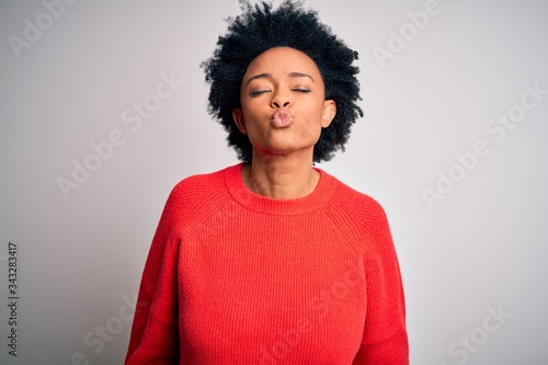 Young beautiful African American afro woman with curly hair wearing red casual sweater looking at the camera blowing a kiss on air being lovely and sexy. Love expression.