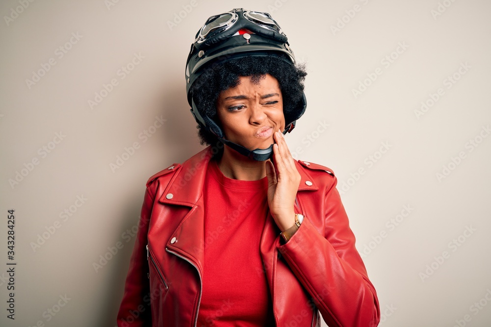 Young African American afro motorcyclist woman with curly hair wearing motorcycle helmet touching mouth with hand with painful expression because of toothache or dental illness on teeth. Dentist Young African American afro motorcyclist woman with curly hair wearing motorcycle helmet touching mouth with hand with painful expression because of toothache or dental illness on teeth. Dentist
