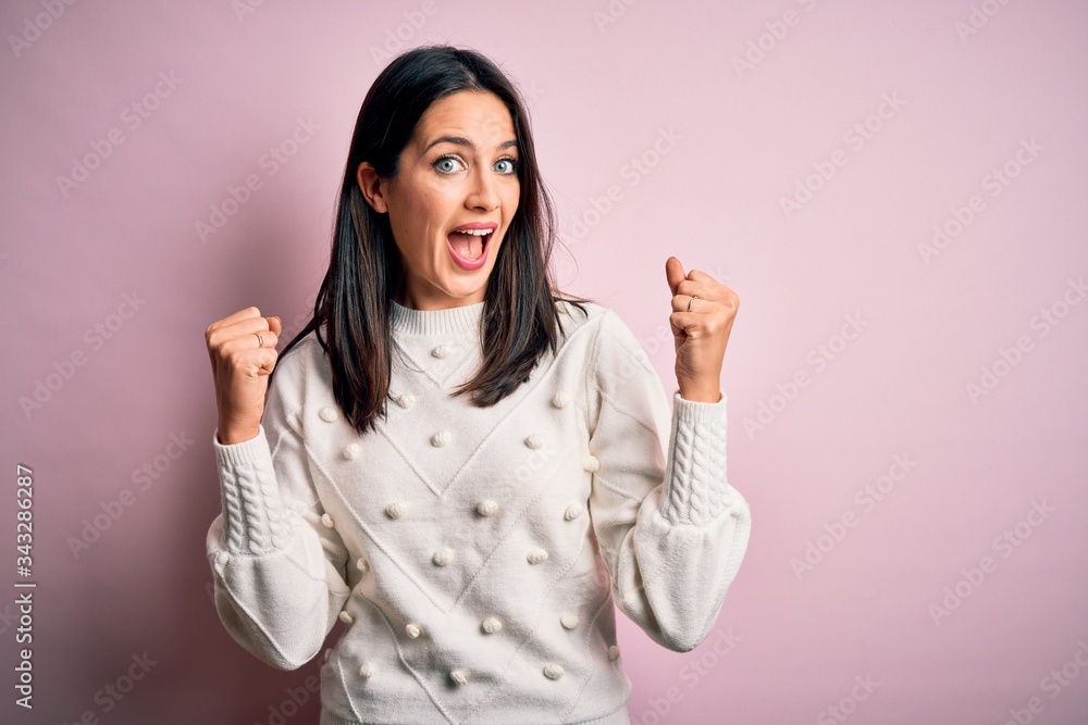 Young brunette woman with blue eyes wearing casual sweater over isolated pink background celebrating surprised and amazed for success with arms raised and open eyes. Winner concept. Young brunette woman with blue eyes wearing casual sweater over isolated pink background celebrating surprised and amazed for success with arms raised and open eyes. Winner concept.