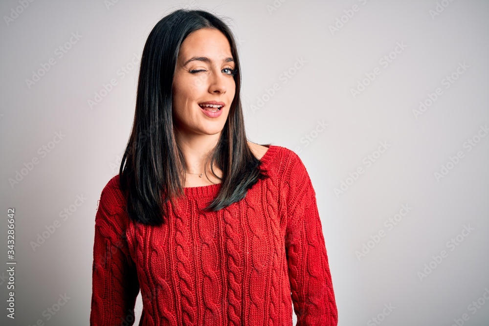 Young brunette woman with blue eyes wearing casual sweater over isolated white background winking looking at the camera with sexy expression, cheerful and happy face. Young brunette woman with blue eyes wearing casual sweater over isolated white background winking looking at the camera with sexy expression, cheerful and happy face.