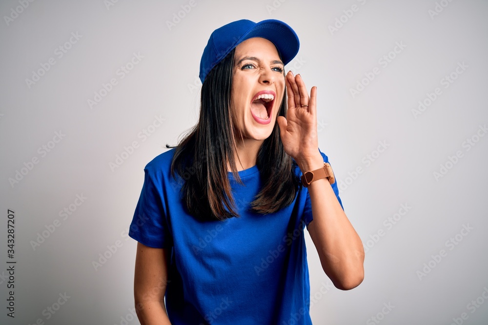 Young delivery woman with blue eyes wearing cap standing over blue background shouting and screaming loud to side with hand on mouth. Communication concept. Young delivery woman with blue eyes wearing cap standing over blue background shouting and screaming loud to side with hand on mouth. Communication concept.