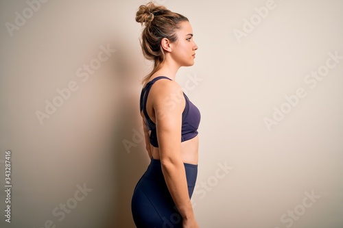 Young beautiful blonde sportswoman doing sport wearing sportswear over white background looking to side, relax profile pose with natural face with confident smile.