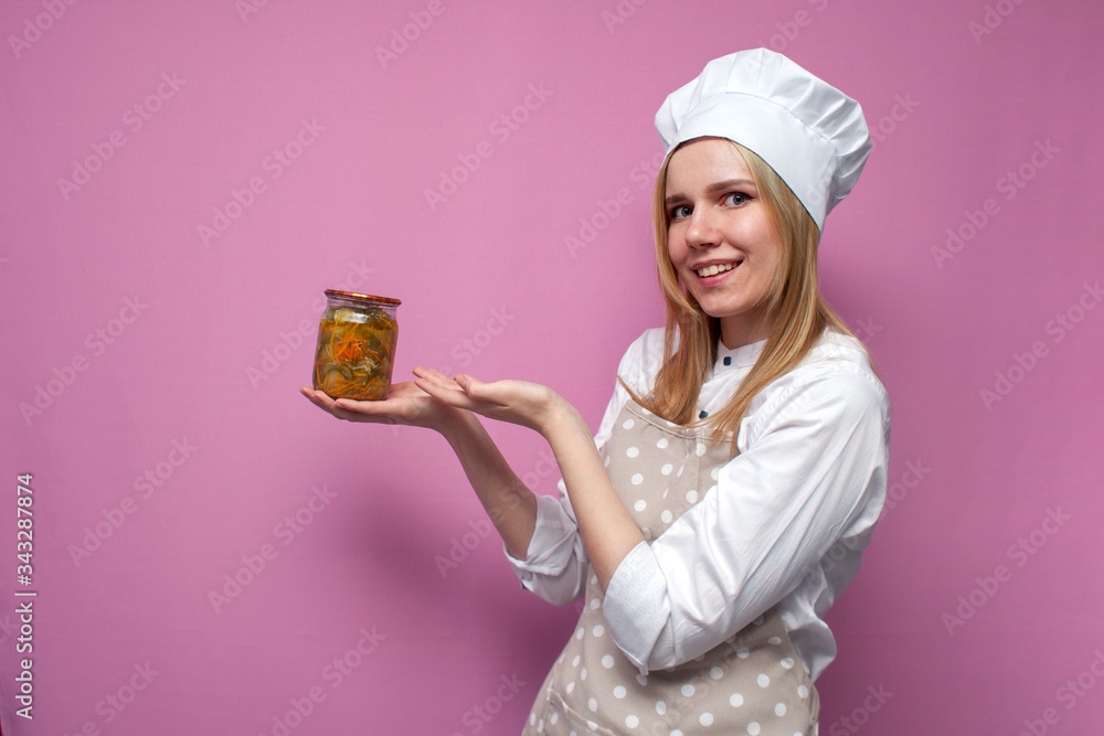 cheerful girl cook in kitchen clothes holds canned food and smiles on a colored background, woman housewife with food blanks, copy space cheerful girl cook in kitchen clothes holds canned food and smiles on a colored background, woman housewife with food blanks, copy space