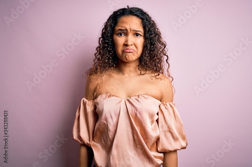Young beautiful woman with curly hair wearing casual t-shirt standing over pink background depressed and worry for distress, crying angry and afraid. Sad expression.
