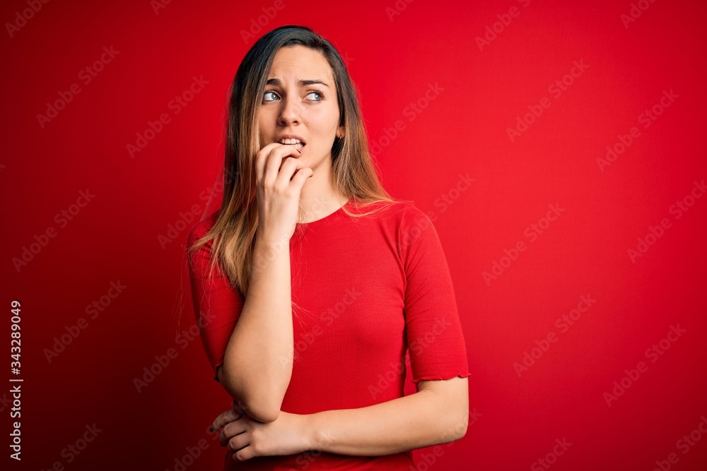 Young beautiful blonde woman with blue eyes wearing casual t-shirt over red background looking stressed and nervous with hands on mouth biting nails. Anxiety problem. Young beautiful blonde woman with blue eyes wearing casual t-shirt over red background looking stressed and nervous with hands on mouth biting nails. Anxiety problem.