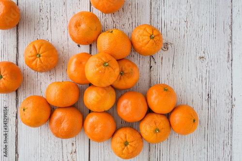 Small clementine oranges spilled onto a whitewashed wood background
