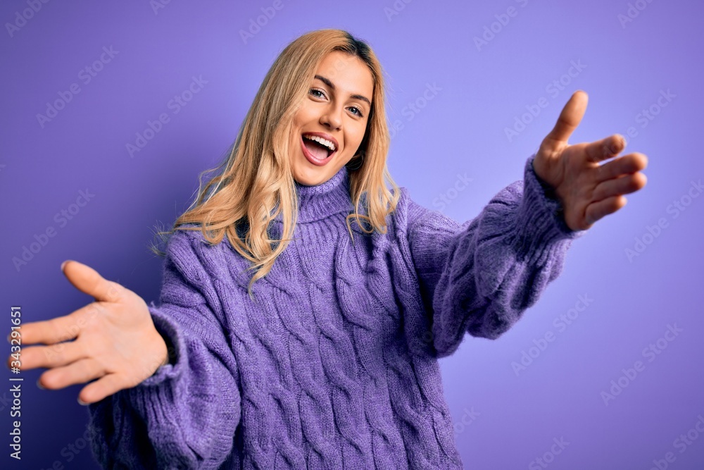 Young beautiful blonde woman wearing casual turtleneck sweater over purple background smiling cheerful offering hands giving assistance and acceptance. Young beautiful blonde woman wearing casual turtleneck sweater over purple background smiling cheerful offering hands giving assistance and acceptance.