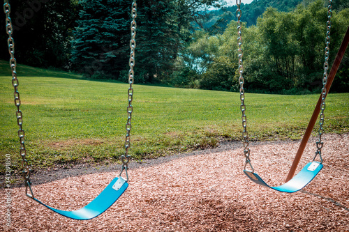 Empty swings on a swingset at a park during the summer