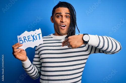 Young african american afro man holding banner with brexit message over blue background with surprise face pointing finger to himself photo