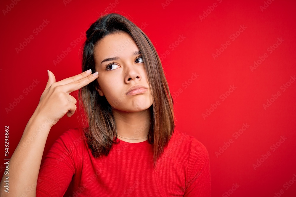 Young beautiful brunette girl wearing casual t-shirt over isolated red background Shooting and killing oneself pointing hand and fingers to head like gun, suicide gesture. Young beautiful brunette girl wearing casual t-shirt over isolated red background Shooting and killing oneself pointing hand and fingers to head like gun, suicide gesture.