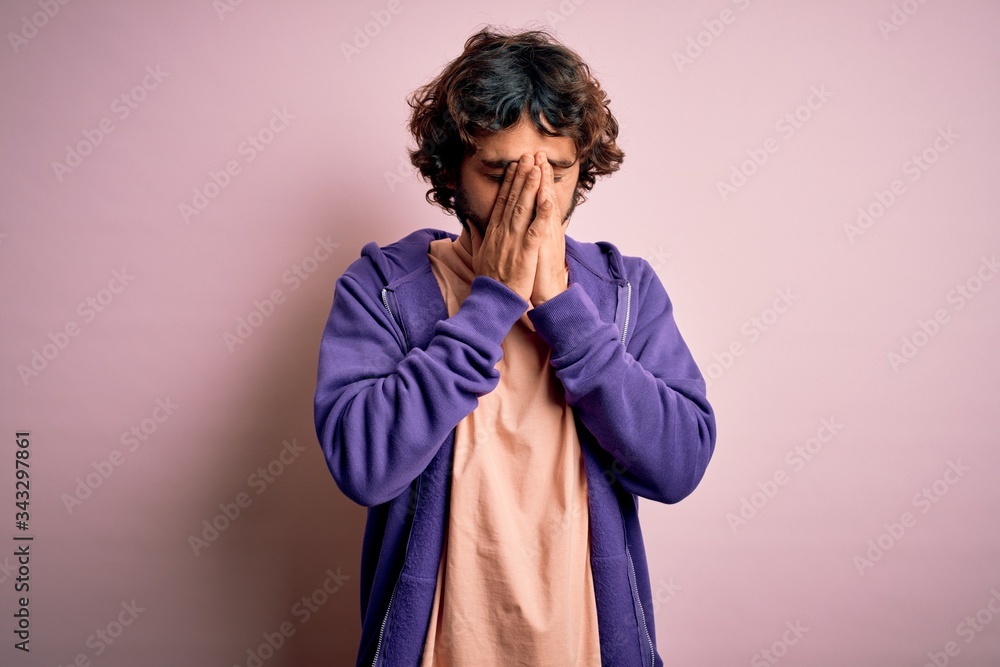 Young handsome sporty man with beard wearing casual sweatshirt over pink background with sad expression covering face with hands while crying. Depression concept. Young handsome sporty man with beard wearing casual sweatshirt over pink background with sad expression covering face with hands while crying. Depression concept.