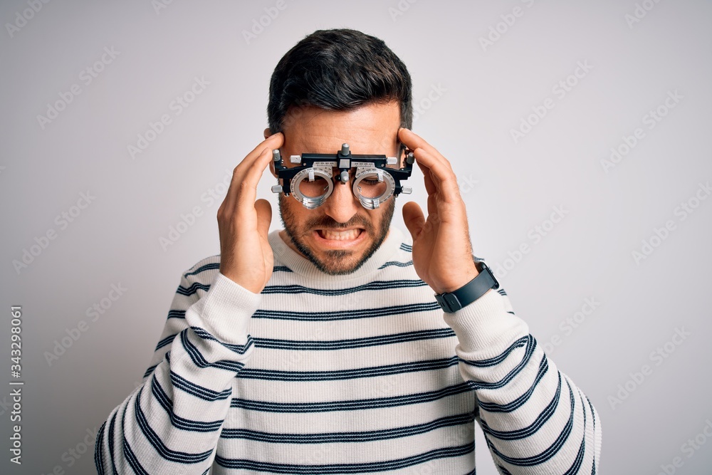 Young handsome man with beard wearing optometry glasses over isolated white background with hand on head for pain in head because stress. Suffering migraine. Young handsome man with beard wearing optometry glasses over isolated white background with hand on head for pain in head because stress. Suffering migraine.