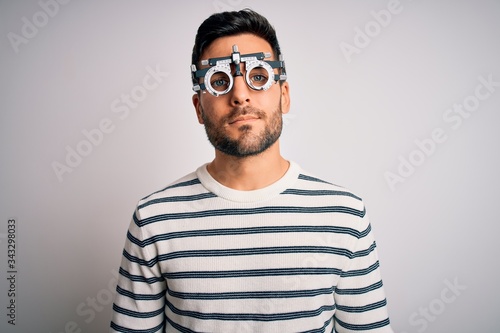 Young handsome man with beard wearing optometry glasses over isolated white background Relaxed with serious expression on face. Simple and natural looking at the camera. © Krakenimages.com