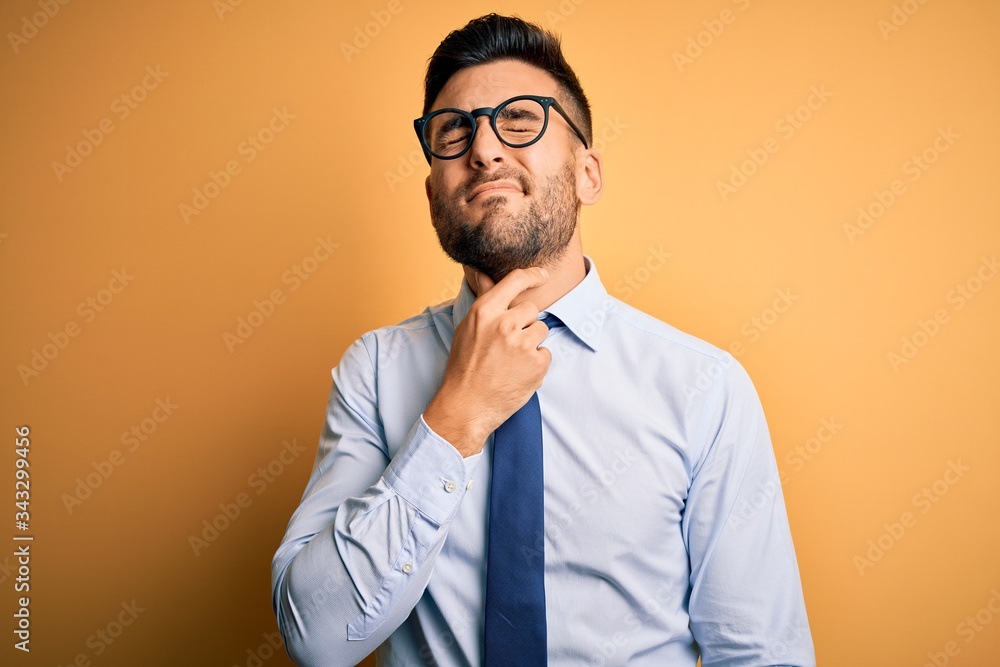 Young handsome businessman wearing tie and glasses standing over yellow background Touching painful neck, sore throat for flu, clod and infection Young handsome businessman wearing tie and glasses standing over yellow background Touching painful neck, sore throat for flu, clod and infection