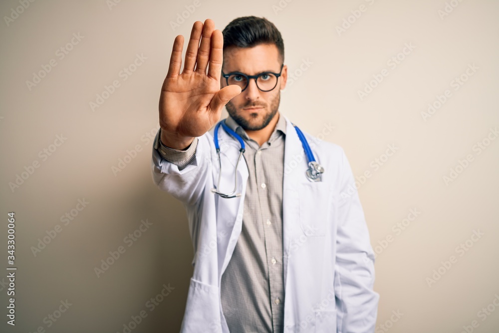 Young doctor man wearing glasses, medical white robe and stethoscope over isolated background doing stop sing with palm of the hand. Warning expression with negative and serious gesture on the face. Young doctor man wearing glasses, medical white robe and stethoscope over isolated background doing stop sing with palm of the hand. Warning expression with negative and serious gesture on the face.