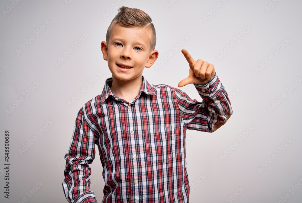 Young little caucasian kid with blue eyes wearing elegant shirt standing over isolated background smiling and confident gesturing with hand doing small size sign with fingers looking and the camera Young little caucasian kid with blue eyes wearing elegant shirt standing over isolated background smiling and confident gesturing with hand doing small size sign with fingers looking and the camera