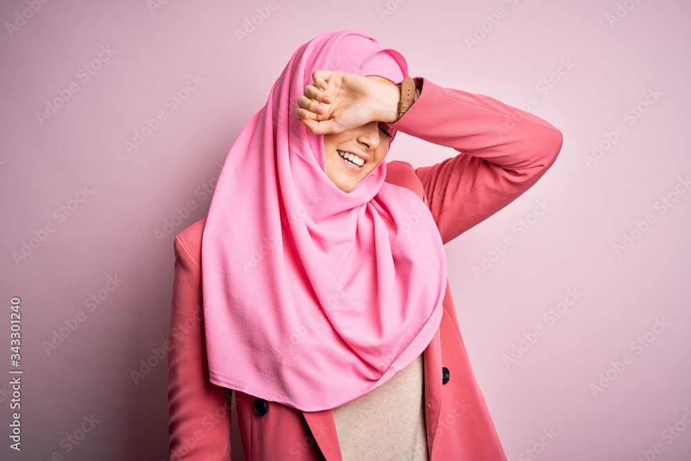 Young beautiful girl wearing muslim hijab standing over isolated pink background covering eyes with arm smiling cheerful and funny. Blind concept. Young beautiful girl wearing muslim hijab standing over isolated pink background covering eyes with arm smiling cheerful and funny. Blind concept.