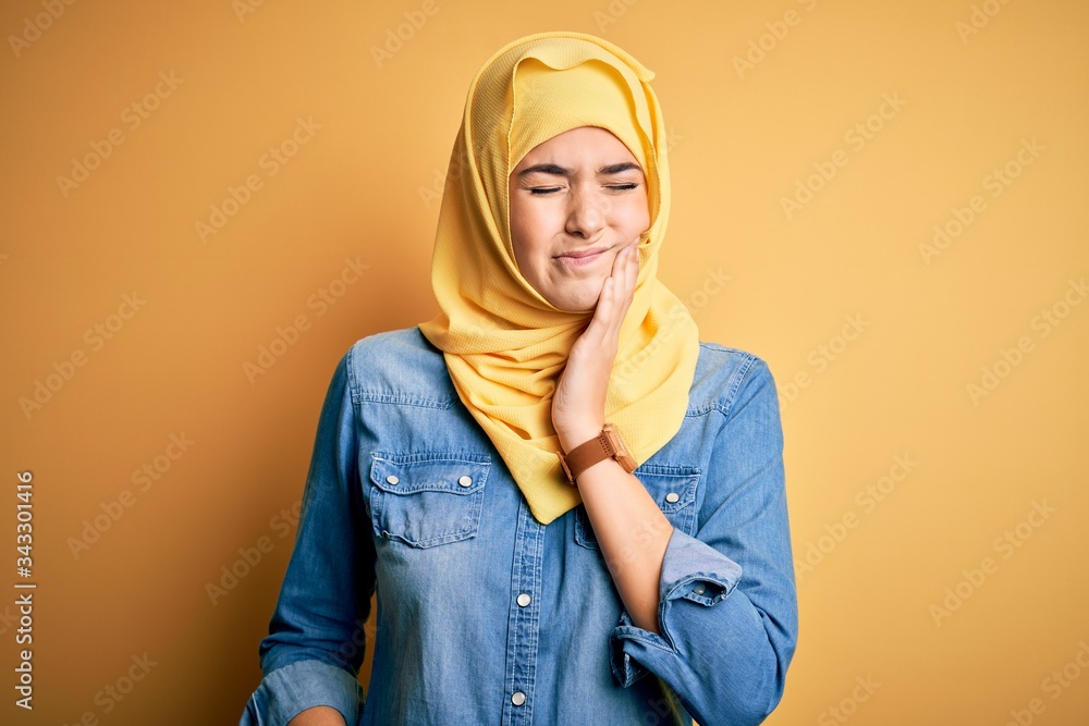 Young beautiful girl wearing muslim hijab standing over isolated yellow background touching mouth with hand with painful expression because of toothache or dental illness on teeth. Dentist Young beautiful girl wearing muslim hijab standing over isolated yellow background touching mouth with hand with painful expression because of toothache or dental illness on teeth. Dentist