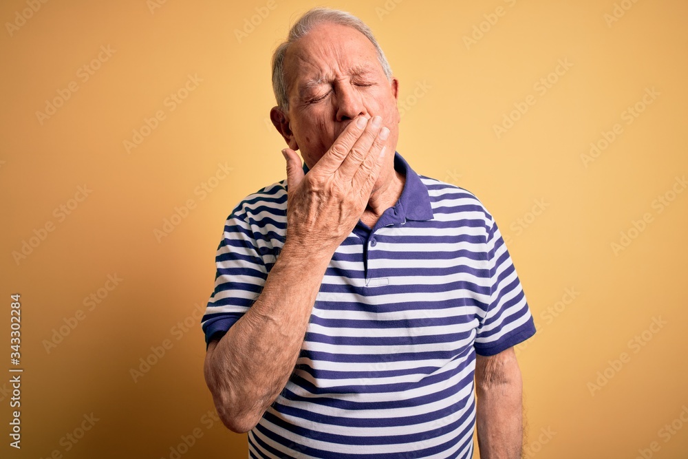 Grey haired senior man wearing casual navy striped t-shirt standing over yellow background bored yawning tired covering mouth with hand. Restless and sleepiness. Grey haired senior man wearing casual navy striped t-shirt standing over yellow background bored yawning tired covering mouth with hand. Restless and sleepiness.