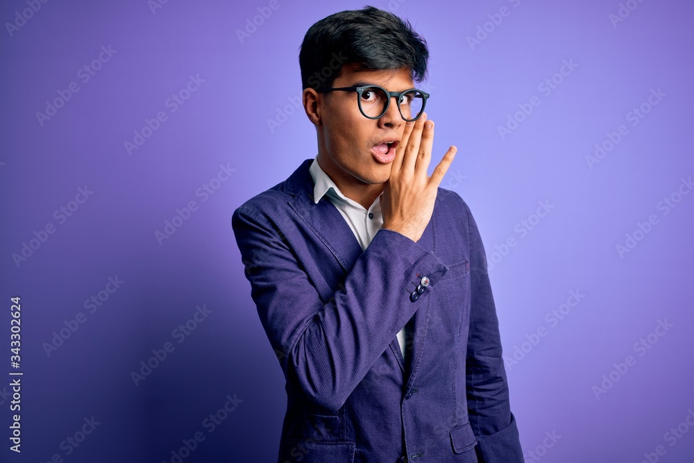 Young handsome business man wearing jacket and glasses over isolated purple background hand on mouth telling secret rumor, whispering malicious talk conversation