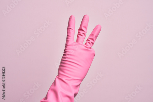 Hand of caucasian young man with cleaning glove over isolated pink background counting number 3 showing three fingers