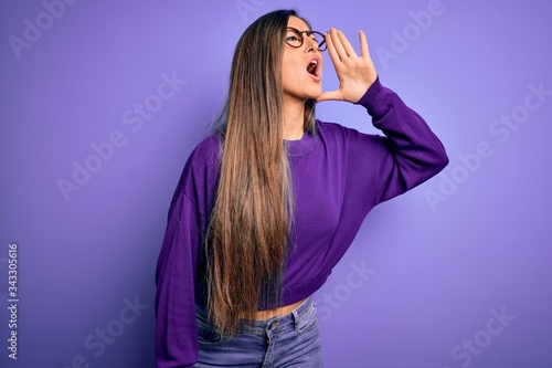 Young beautiful smart woman wearing glasses over purple isolated background shouting and screaming loud to side with hand on mouth. Communication concept.