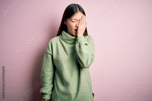 Young beautiful asian woman wearing green winter sweater over pink solated background Yawning tired covering half face, eye and mouth with hand. Face hurts in pain. © Krakenimages.com