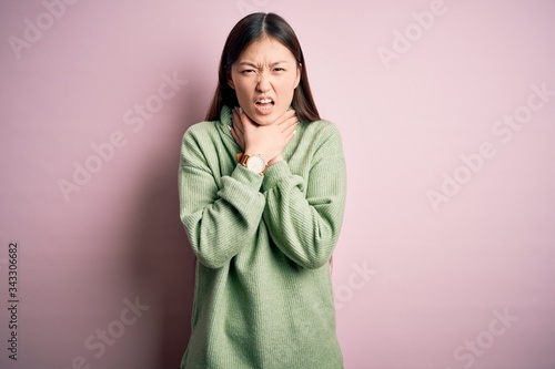 Young beautiful asian woman wearing green winter sweater over pink solated background shouting suffocate because painful strangle. Health problem. Asphyxiate and suicide concept. © Krakenimages.com