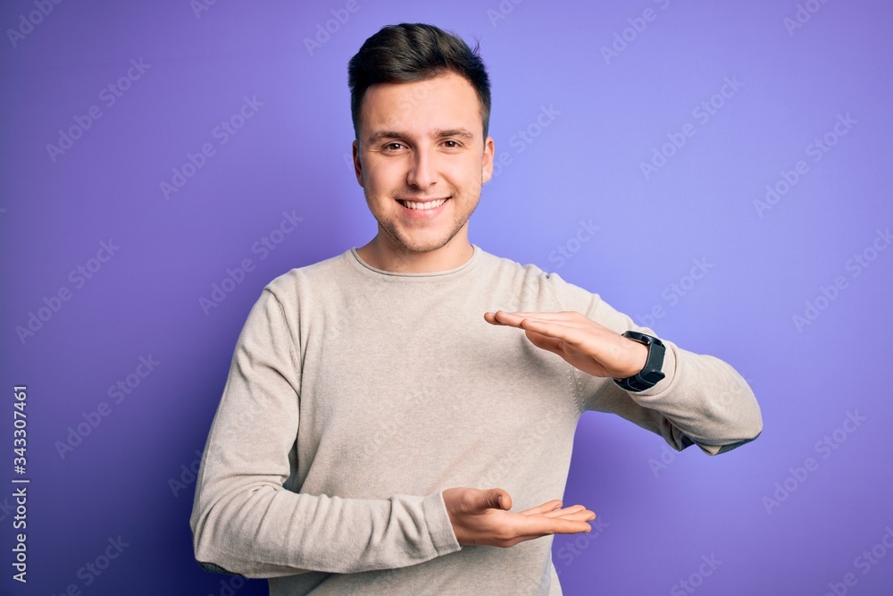 Young handsome caucasian man wearing casual sweater over purple isolated background gesturing with hands showing big and large size sign, measure symbol. Smiling looking at the camera. Measuring Young handsome caucasian man wearing casual sweater over purple isolated background gesturing with hands showing big and large size sign, measure symbol. Smiling looking at the camera. Measuring