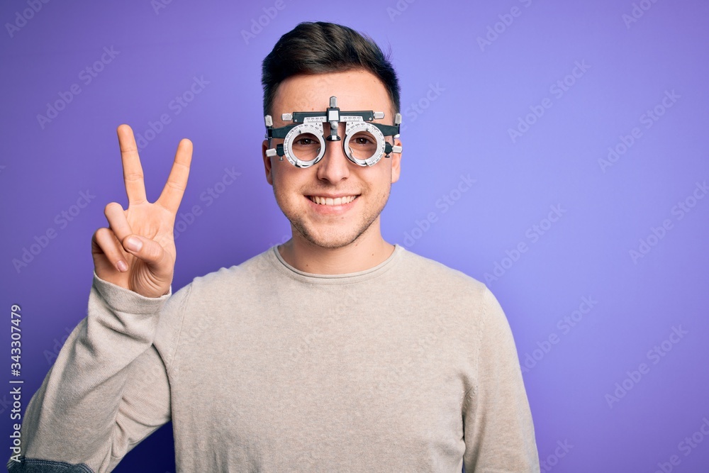 Naklejka premium Young handsome caucasian man wearing optometrical glasses over purple background smiling with happy face winking at the camera doing victory sign. Number two.